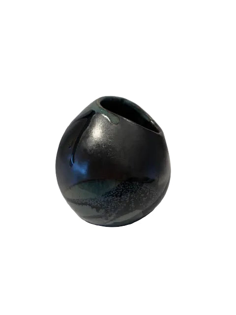A small glossy ceramic vase with a rounded, bulbous shape and a small opening at the top, featuring a dark iridescent glaze with blue, green, and black tones, photographed against a plain white background.