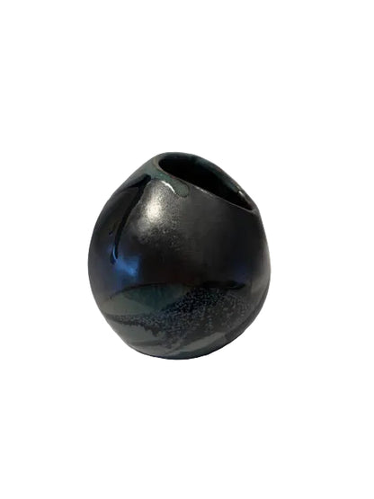 A small glossy ceramic vase with a rounded, bulbous shape and a small opening at the top, featuring a dark iridescent glaze with blue, green, and black tones, photographed against a plain white background.
