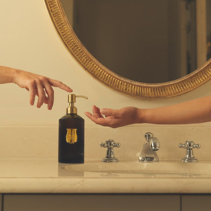 Hands using the Trudon Medie soap pump on a marble vanity beneath a gilt round mirror